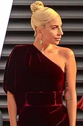 A picture of Lady Gaga in a burgundy one-shoulder dress, looking to the right.