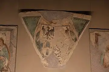 Triangle on which a shield is painted. The latter is divided into four. On the first part on the upper left there is a black bird on a white background, the same on the upper right but erased, on the lower left there is a white castle on a blue background and the last drawing is barely visible.