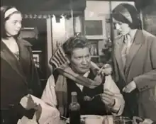 Still from the film showing Alfie Bass a Bindle seated at a table eating, with (standing) his wife on his left and his daughter on the right.