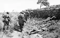 A black and white photograph of a German paratrooper patrol passing several bodies
