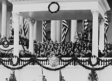 President Coolidge faces Chief Justice Taft. Both have their hands raised as the Oath of Office is delivered. A large crowd stands behind them.