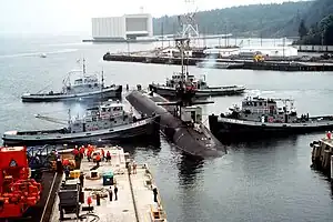 Naval Submarine Base Bangor with tug Mishawaka (rear left) and three other Natick-class tugs guiding the USS&nbsp;Ohio&nbsp;(SSGN-726) out of dry dock at Delta Pier