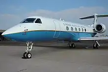 Small jet aircraft built by Gulfstream Aerospace; private executive versions are branded the Gulfstream V, and the Federal Government-owned version depicted here is designated the C-37A. The specific aircraft is named "Normandy" and is painted in VIP livery, with a fuselage painted white on the upper surface and light blue on the lower surface, separated by a thin gold beltline encircling the aircraft. "United States of America" is painted above the six round passenger windows on either side.