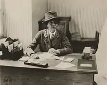 A white woman, smiling broadly, wearing a brimmed hat, necktie, uniform jacket.