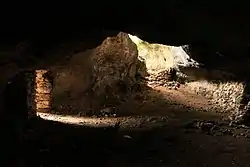 A large cave showing two exits, the top one being natural and the one on the left being walled.