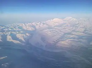 Aerial photo of the Denali and the snowy Alaska Range with a glacier leading to a river