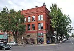 Photograph of the New Logus Block, a red brick building; Picnic tables with umbrellas dot the sidewalk.