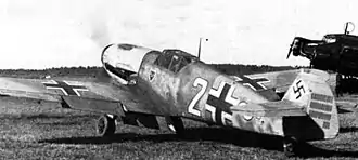 A black and white photograph a propeller driven fighter aircraft viewed from the rear-left. The aircraft is on a grass field, engine appears to be running. It bears three black and white crosses, two on the upper wings and one on the left side of the fuselage besides a large number "2". The tail rudder shows a black swastika plus rudder bears approximately 33 small vertical black lines arranged in three groups of varying length.
