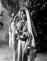 Image 7A young woman from Ramallah, c. 1898-1914. Until the 1940s, women of Palestine wore elaborate handcrafted garments. The creation and maintenance of these items played a significant role in their lives. A knowledgeable observer could determine a woman's village of origin and social status from her clothing. The circular band near this woman's forehead is a ring of coins made from a portion of her dowry money, and indicates that she is unmarried.'Ali Ra'if Efendi, (edited by Durova)