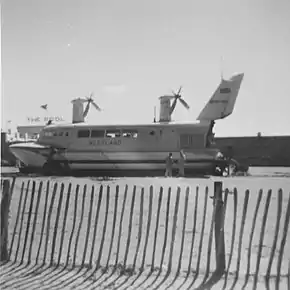 Passenger hovercraft resting on beach adjacent to swimming complex seawall in background behind a safety cordon made from paling fence