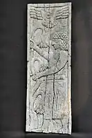 Standing man holding branches of lotus flowers. The winged god Assur appears above.