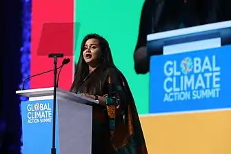 Wickramanayake is speaking at a podium, and the podium has a blue banner reading "Global Climate Action Summit"